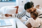 Woman holding her baby on her lap with laptop open on tabletop: How to keep up with your career when you're a new mom