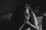 Black and white image of woman with hands over her face filled with negative feelings