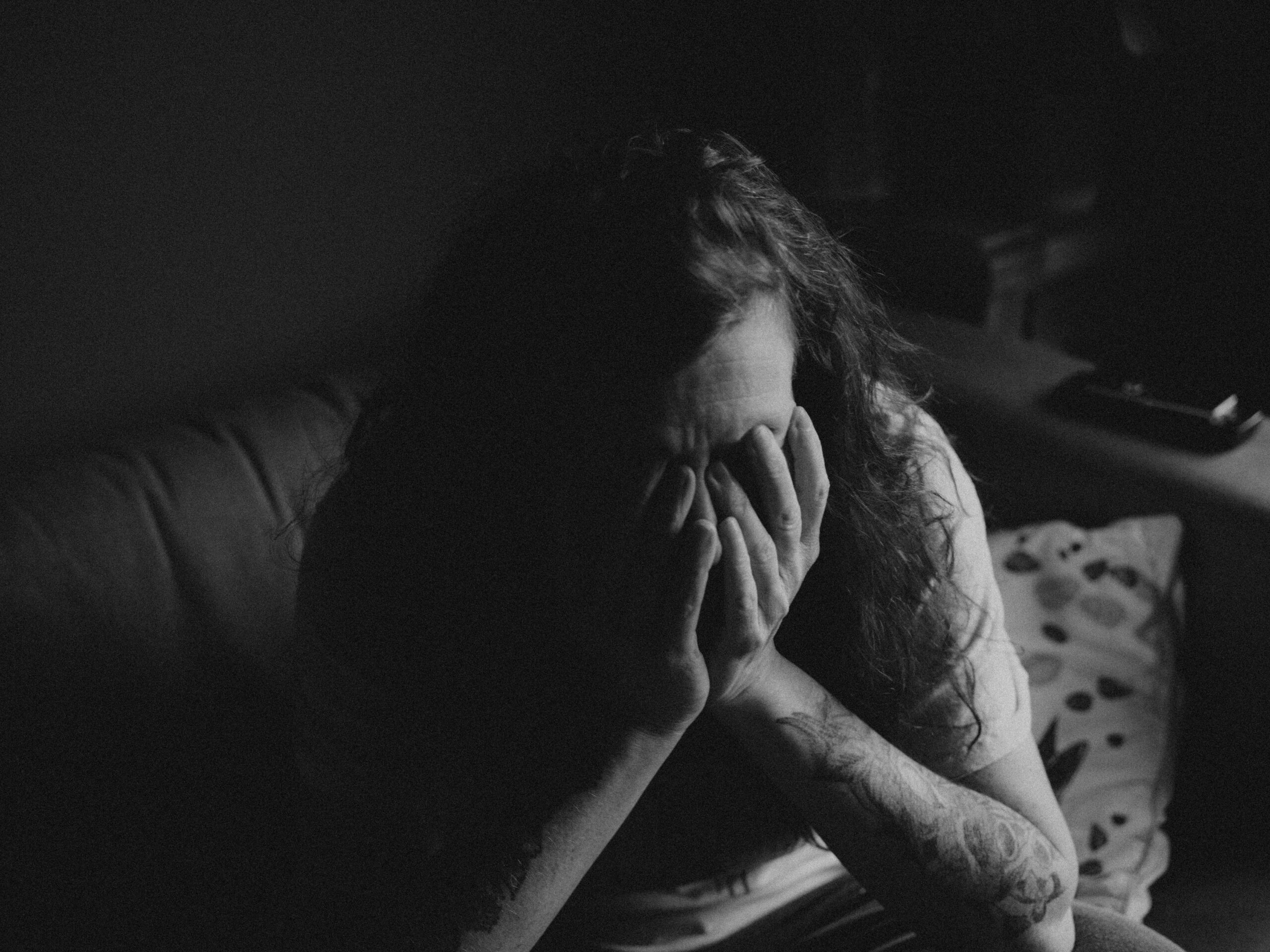 Black and white image of woman with hands over her face filled with negative feelings