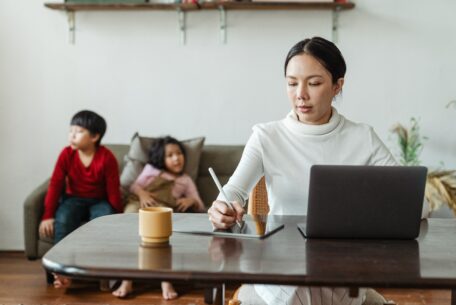 Mother working on laptop with two children in the background: Organized parenting