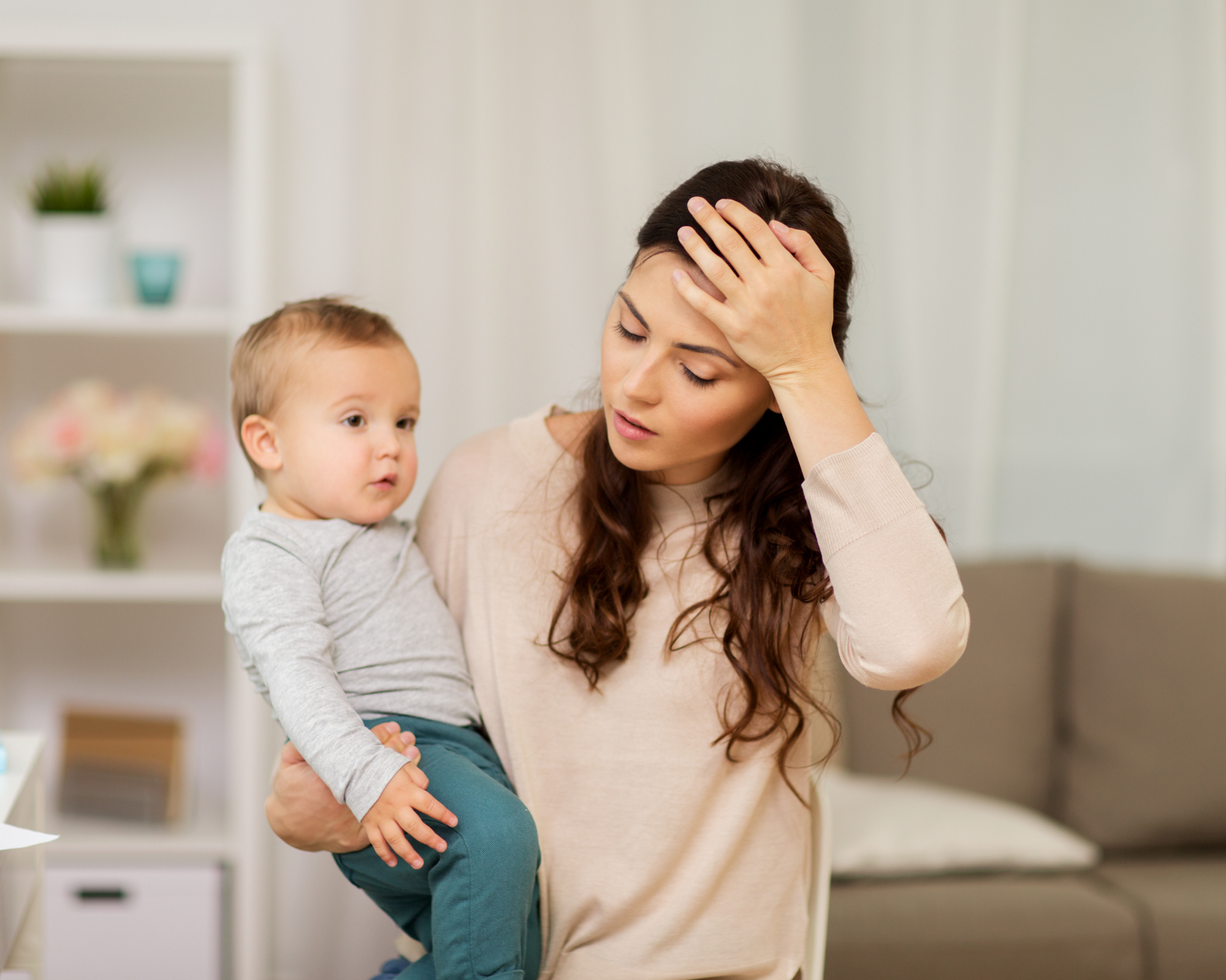 Parental burnout: Mother holding baby while resting her hand against her forehead in show of discomfort