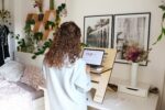 Woman with her back to the camera looking at a laptop while next to her bed: WFHM tips