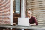 woman sitting and holding white Acer laptop near brown wooden wall: cope with stress of working for yourself