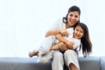 Mother sitting on grey couch with daughter in her lap: encourage your child