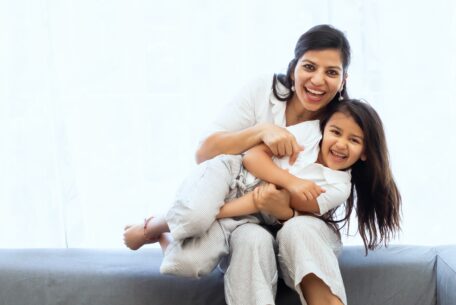 Mother sitting on grey couch with daughter in her lap: encourage your child