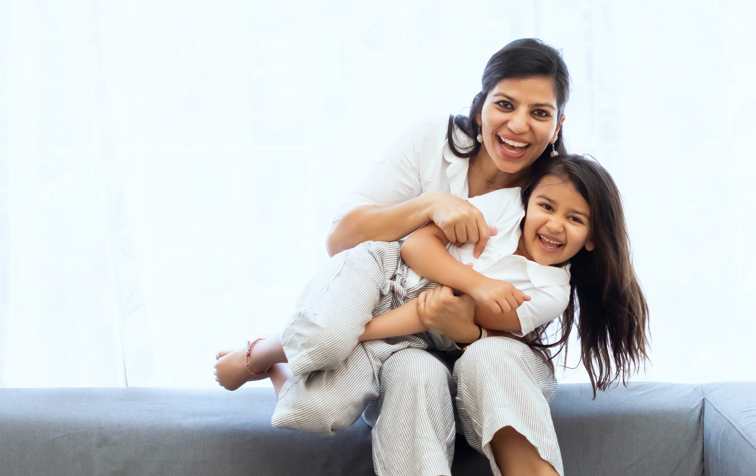 Mother sitting on grey couch with daughter in her lap: encourage your child